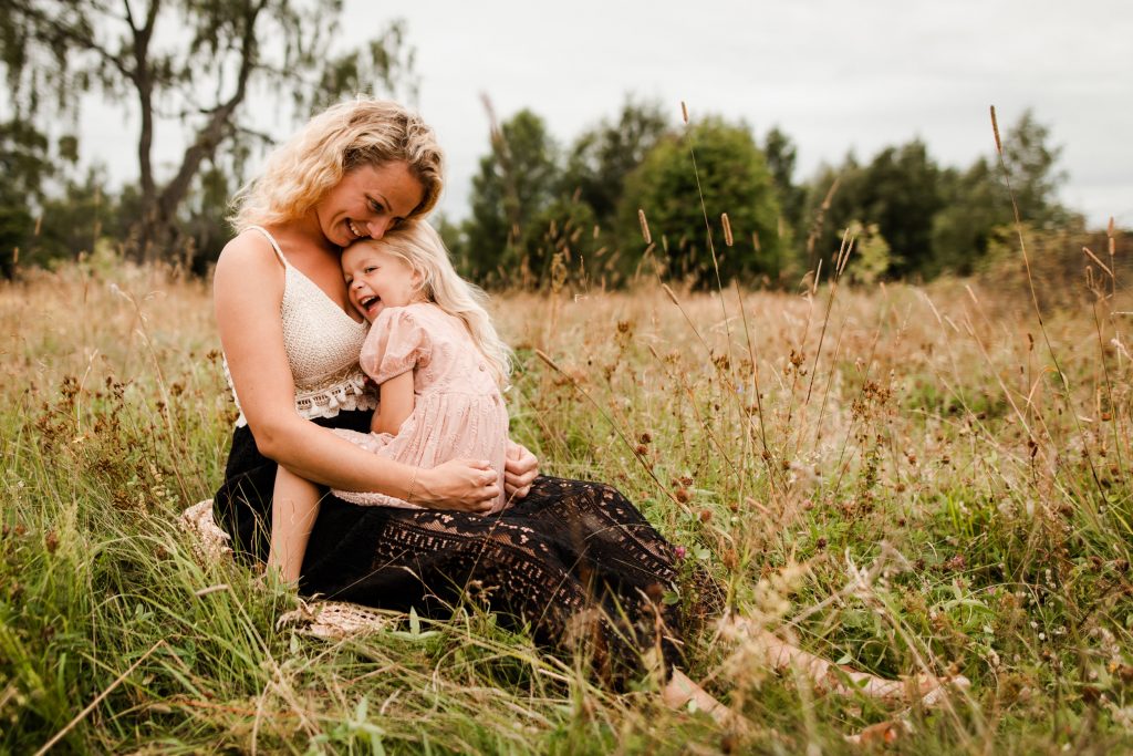 En mamma håller sitt barn i sitt knä och kramas utomhus på en familjefotografering.