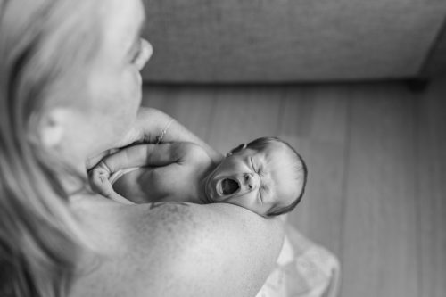 Bebis gäspar i sin mammas famn under en nyföddfotografering i Småland.