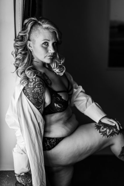 Plus size kvinna i svarta underkläder och vit skjorta på en boudoirfotografering