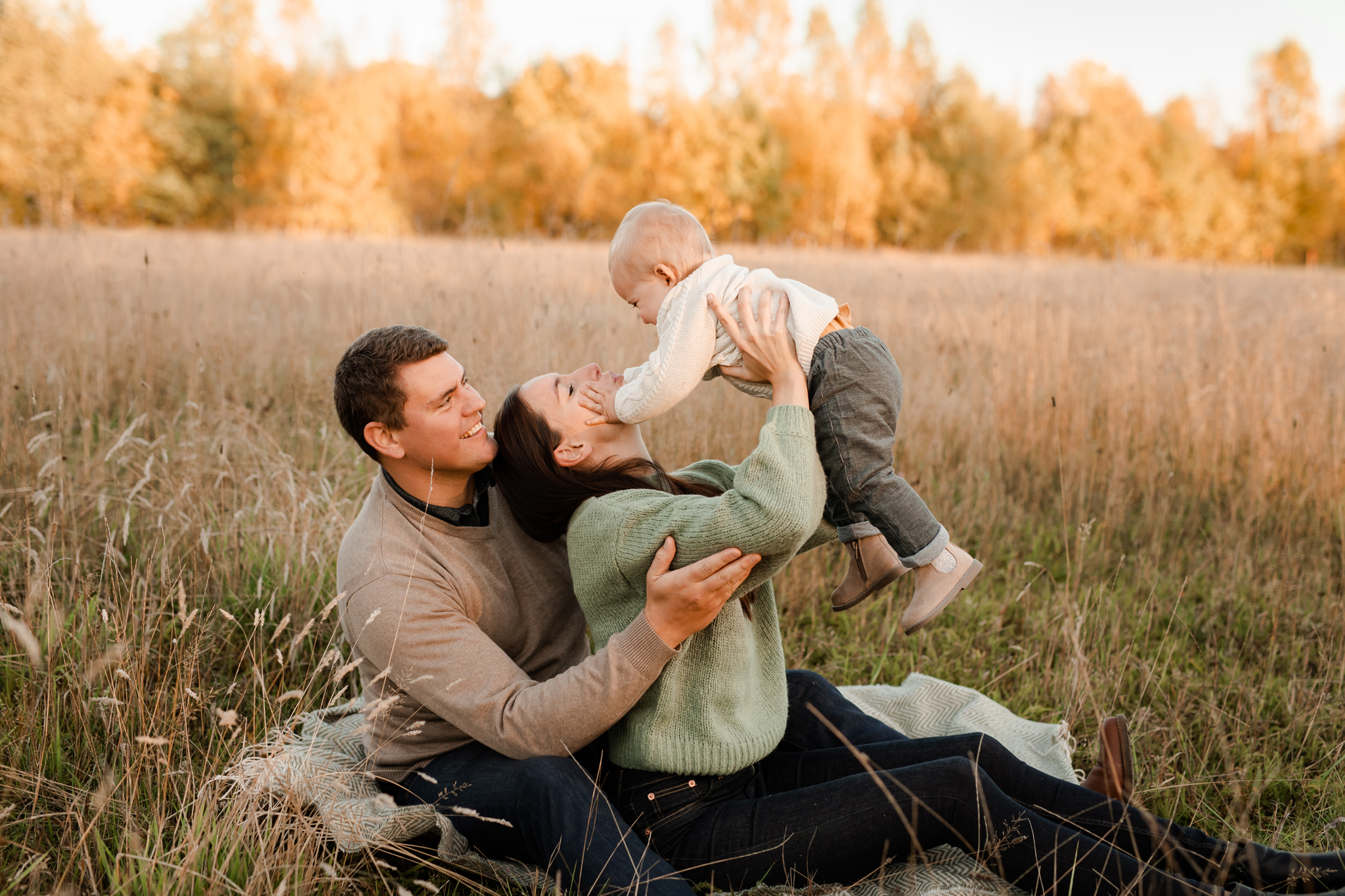 En mamma och en pappa busar med sin ettåriga son på ett fält i solnedgången