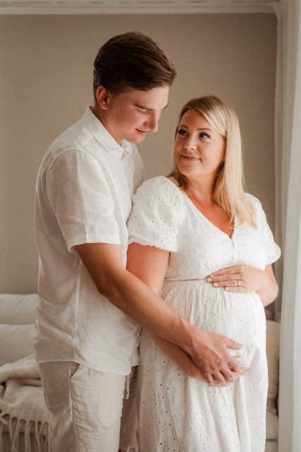 Gravid kvinna blir omhållen av blivande pappan som håller handen på magen