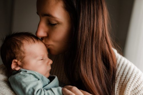 Nybliven mamma pussar på sin nyföddabebis under en nyföddfotografering i Stockholm