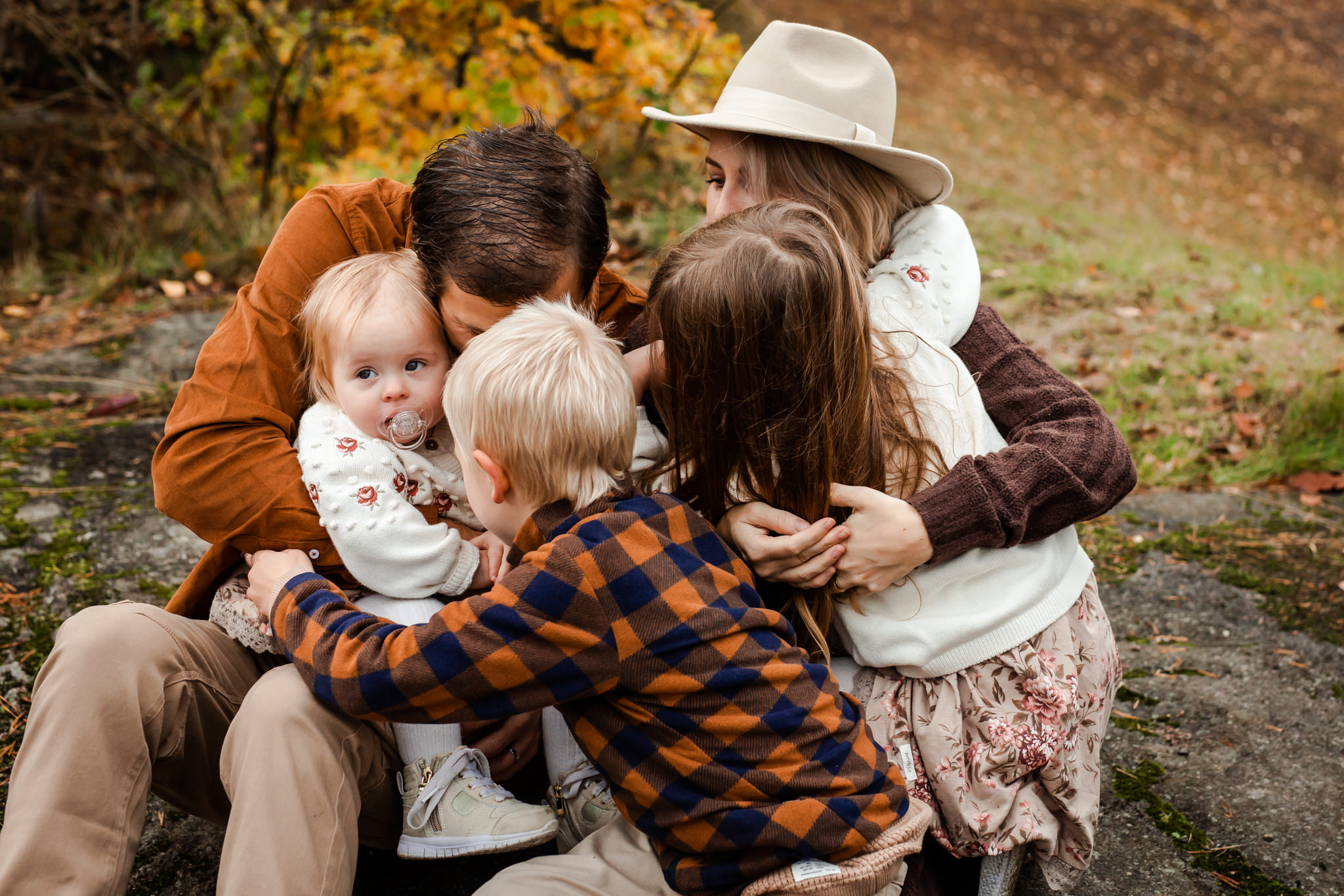 En familj på fem kramas utomhus på sin familjefotografering.