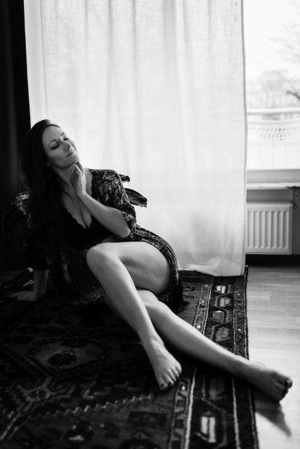 Svartvit bild på en kvinna i kimono som sitter på en röd matta under en boudoirfotografering i Stockholm