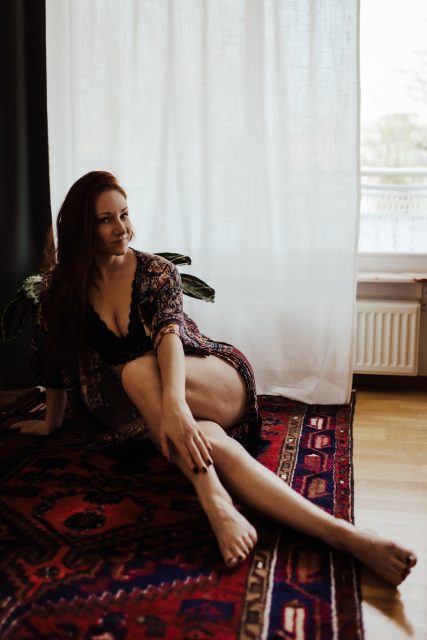 Kvinna i kimono sitter på en röd matta under en boudoirfotografering i Stockholm