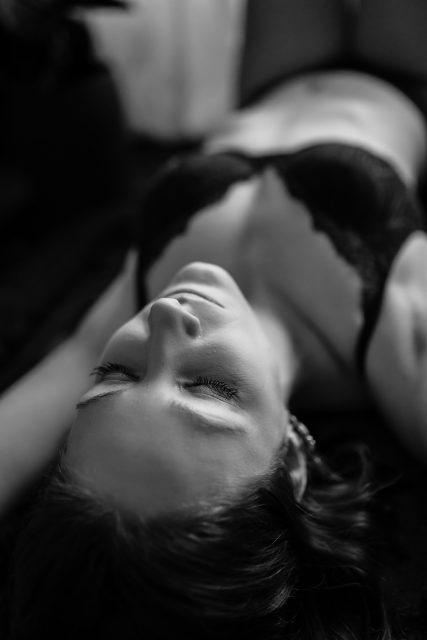 Kvinna i svarta underkläder ligger ner under en boudoirfotografering i Stockholm