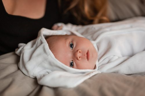 Nyfödd bebis ligger på säng och tittar in i kameran