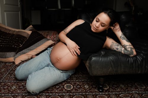 En gravid kvinna sitter på golvet och håller om sin gravidmage och tittar på den