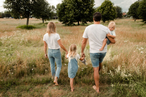 En familj på fyra går hand i hand på ett stort fält iklädda jeans och vita t-shirts på sin familjefotografering i Småland