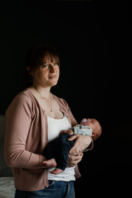 Een mamma håller sin nyfödda bebis sovandes i famnen under en nyföddfotografering i Småland