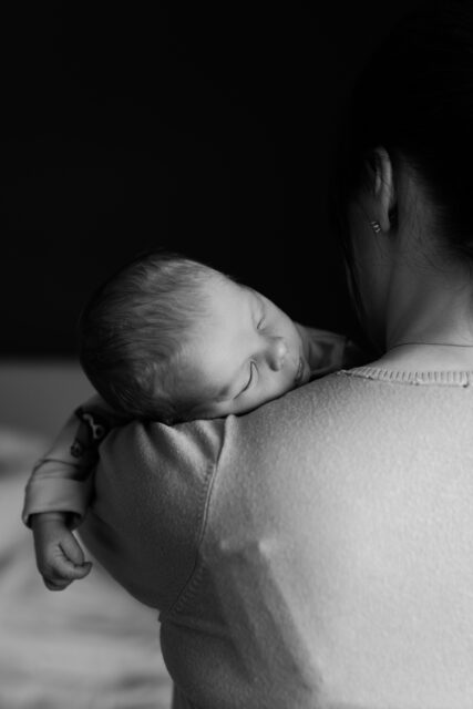 Kvinna håller sin sovande nyfödda bebis på axeln under en nyföddfotografering i Småland.