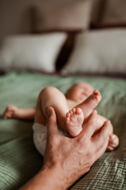 En pappas hand håller i sin nyfödda bebis fötter under en nyföddfotografering i Småland