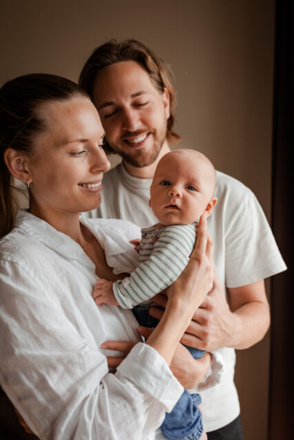 En mamma och en pappa håller sin lilla bebis och tittar på honom under en nyföddfotografering i Småland