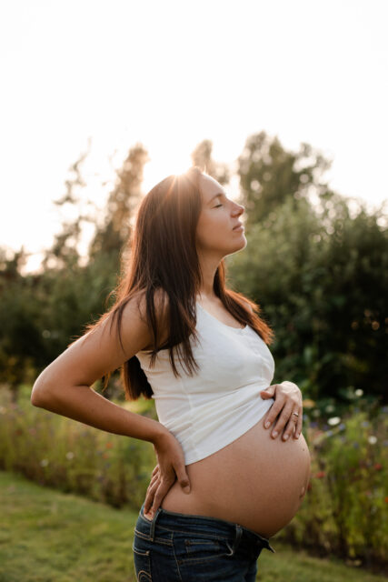 Gravid kvinna står i solnedgången och smeker sin gravida mage.