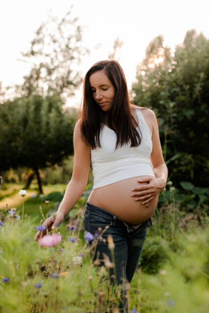 Gravid kvinna går vid ett blomsterhav med ena handen på magen