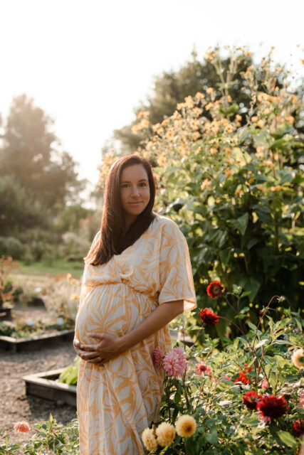 Gravid kvinna smeker sin mage i ett blomsterhav med dahlior