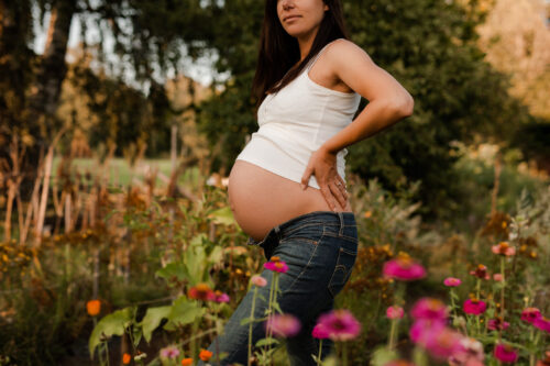 Gravid kvinna står utomhus vid ett blomsterhav.