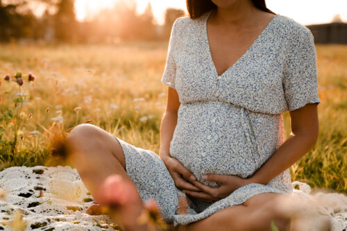 Gravid kvinna sitter på ett fält med ängsblomster.