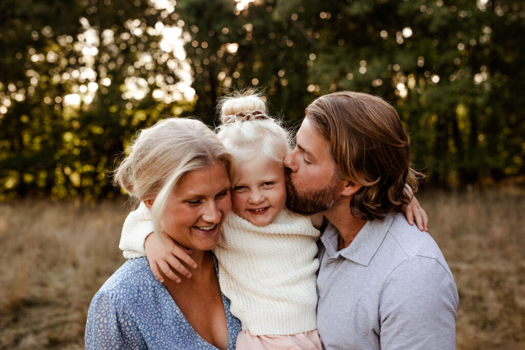 En mamma och en pappa håller sitt barn mellan sig och busar.