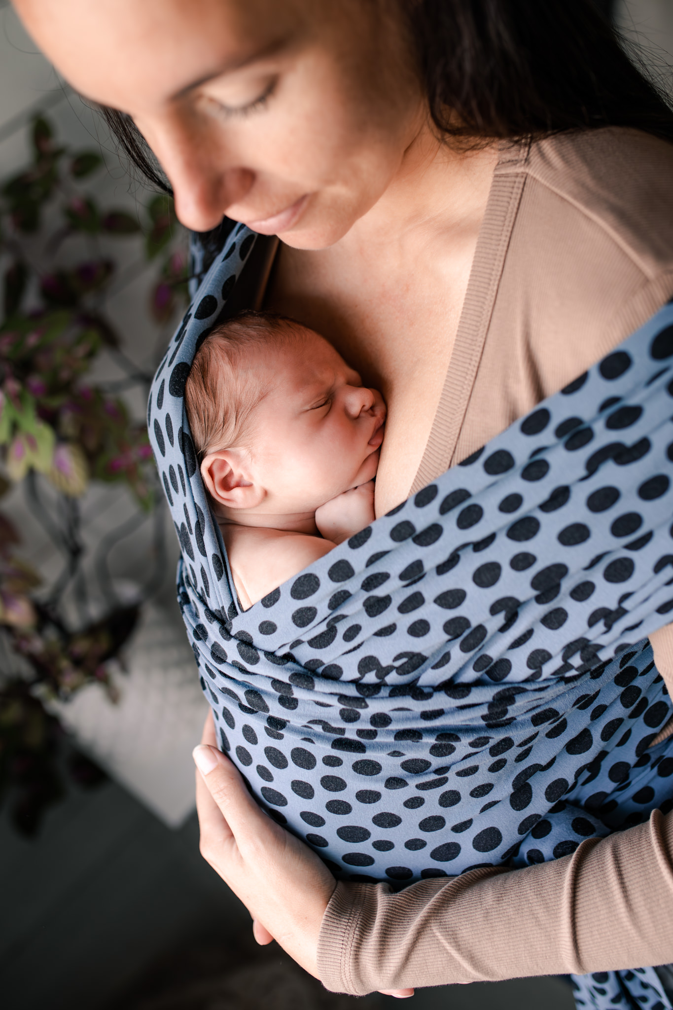 En mamma bär sin nyfödda bebis i en Coracor bärsjal för hud mot hud kontakt.