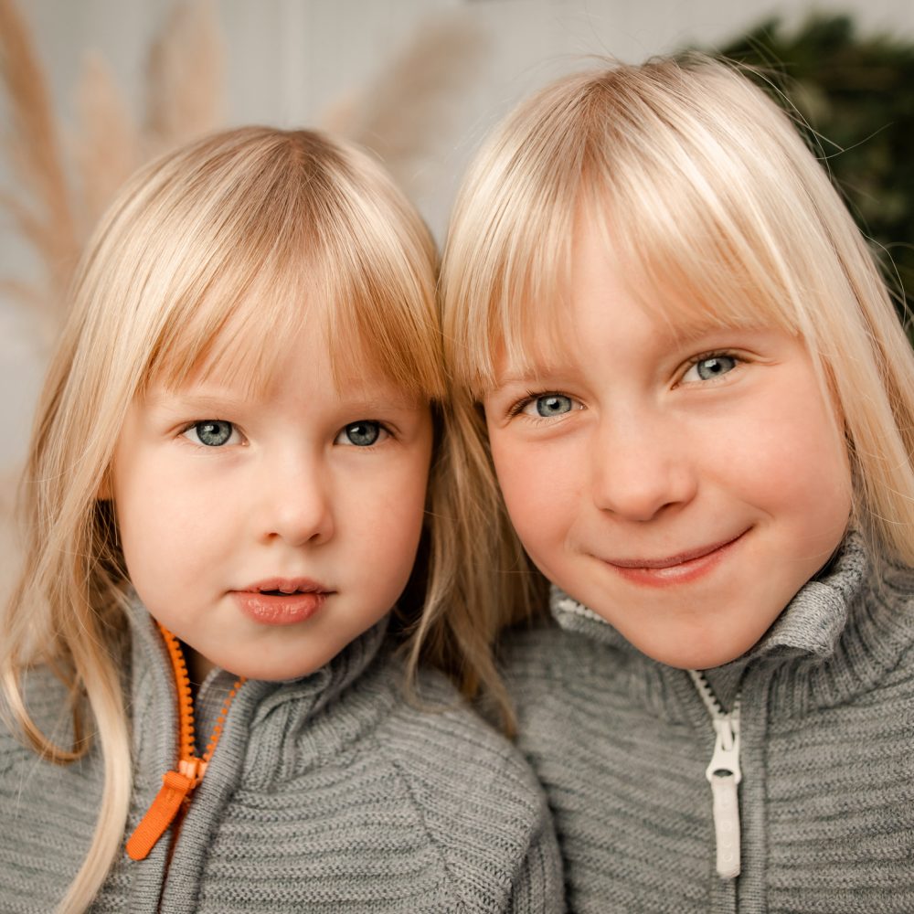 Två blonda systrar tittar in i kameran under en barnfotografering i Eksjö.