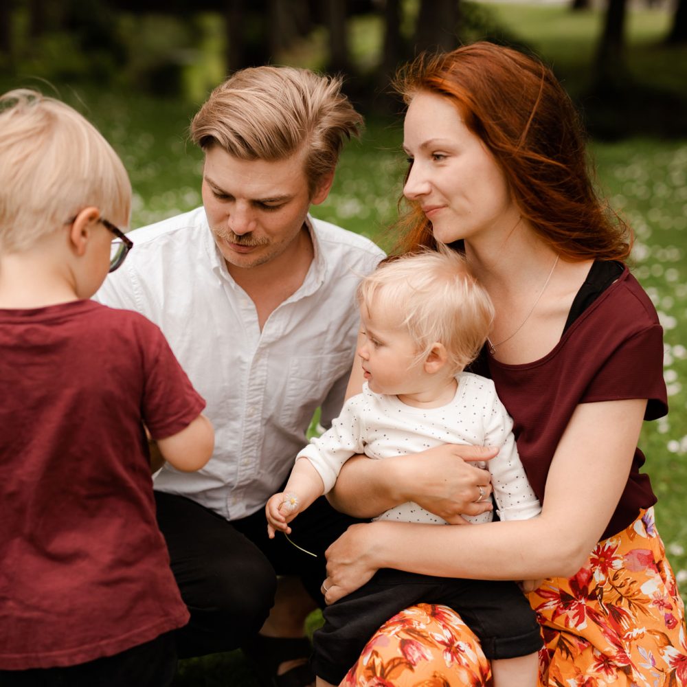 En pappa, mamma och två barn sitter på gräset på sin familjefotografering